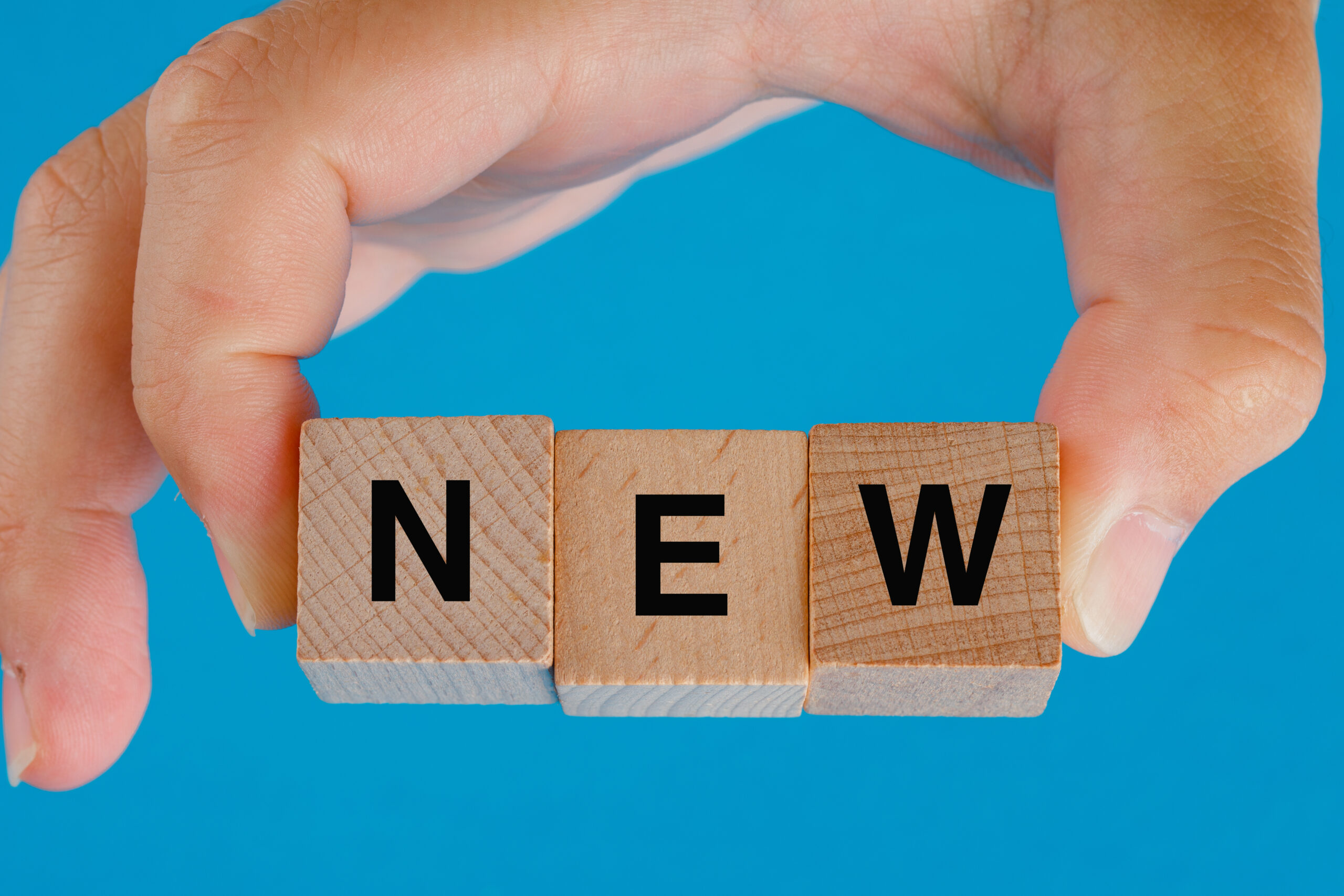 business idea concept blue table side view hand holding wooden cubes with word new scaled