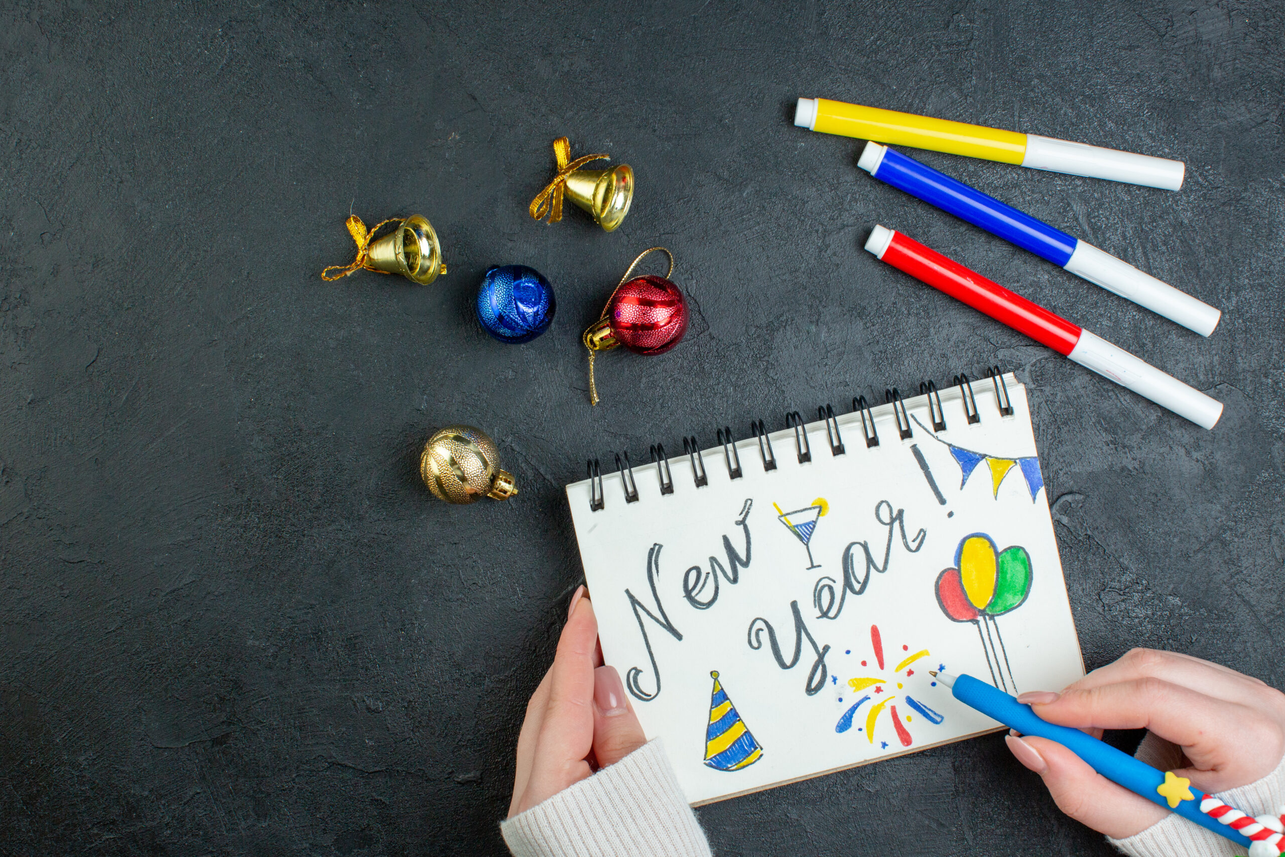 top view hand holding pen spiral notebook with new year writing drawings decoration accessories black background scaled